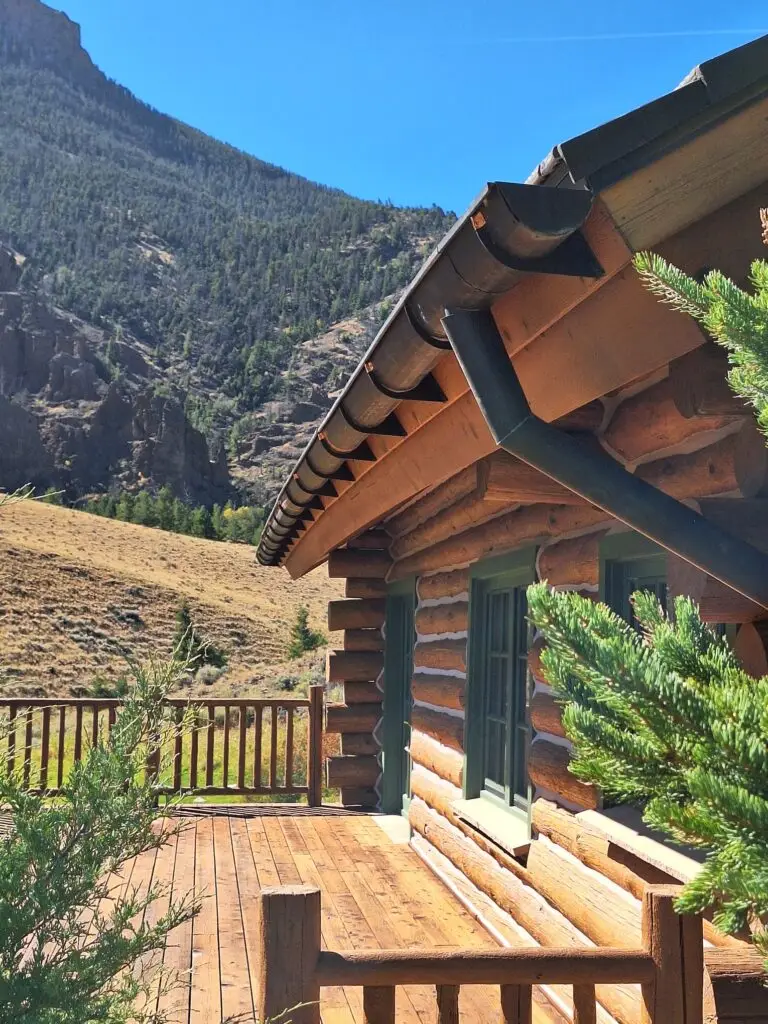 Exterior view of a log cabin featuring newly installed metal gutters and downspouts overlooking Wyoming mountain scenery.