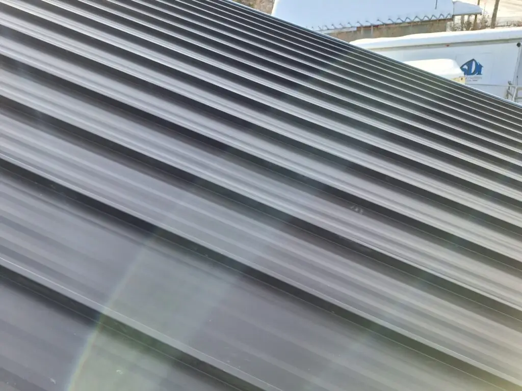 Close-up view of a dark-colored metal roof with ribbed panels reflecting sunlight.