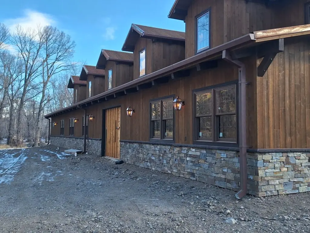 Large rustic lodge-style building with wood siding, stone wainscoting, and custom exterior finishes completed by Bald Ridge Enterprises in Wyoming’s mountain region.
