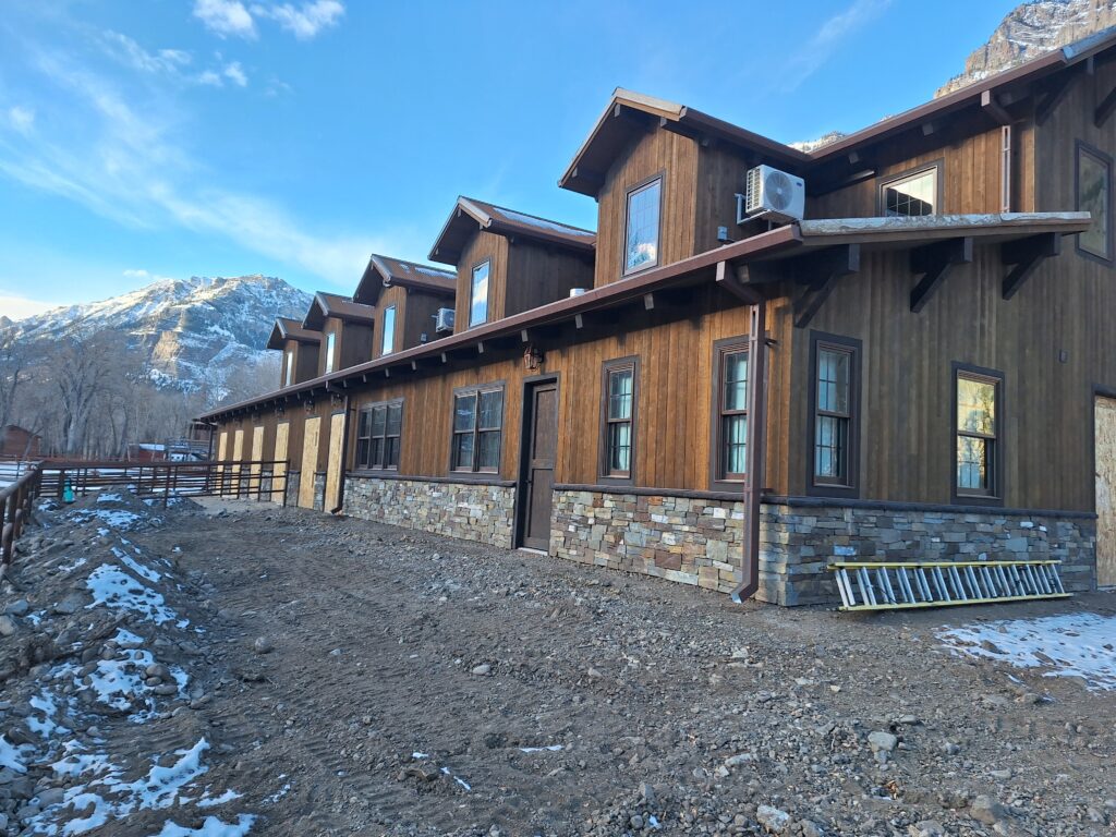 Large rustic lodge-style building with wood siding, stone wainscoting, and custom exterior finishes completed by Bald Ridge Enterprises in Wyoming’s mountain region.