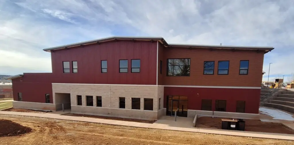Exterior view of a two-story commercial building with red metal siding, tan block lower walls, and multiple windows during construction.