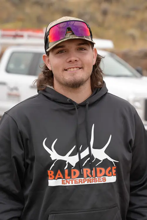 An employee wearing a black “Bald Ridge Enterprises” hoodie and reflective sunglasses smiles outdoors with a company work truck in the background.
