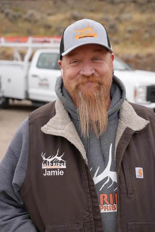 Bald Ridge employee wearing a brown vest and cap, smiling outdoors with a white work truck behind him.