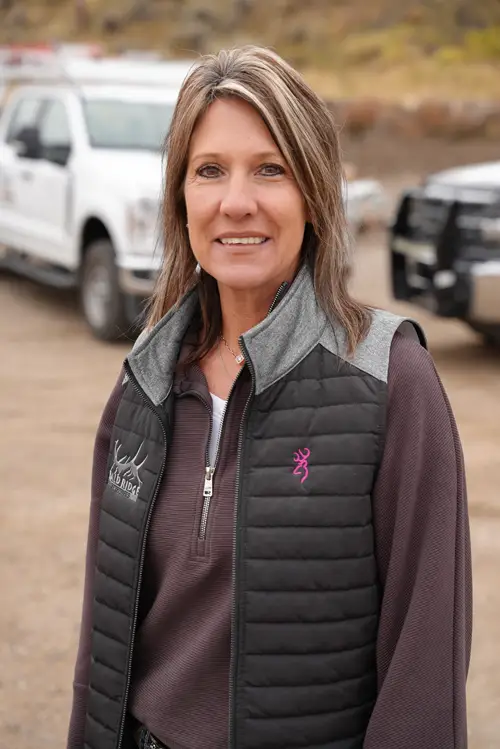 Bald Ridge employee in a black jacket smiling outdoors with trucks in the background.