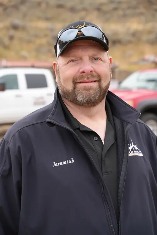 Bald Ridge employee wearing a cap and sunglasses smiling with white company trucks behind him.