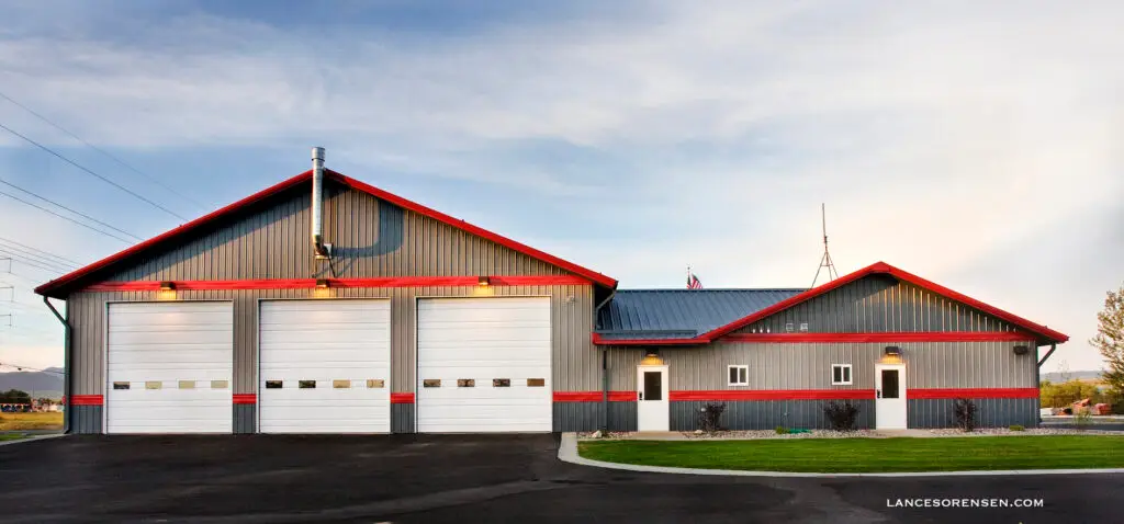 A modern gray metal fire station with red trim and three large white garage doors under an evening sky.